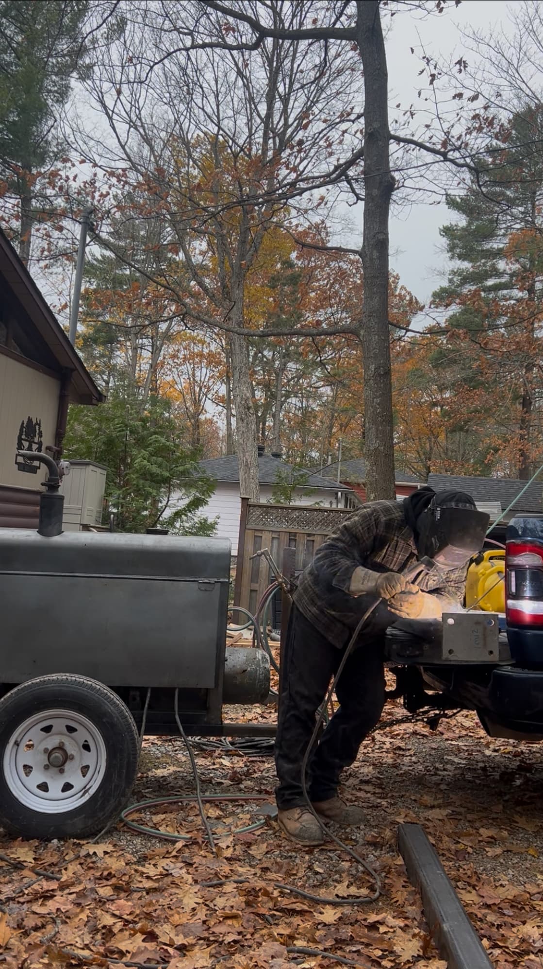 Welder in protective gear works on a truck bed beside a portable welding machine.