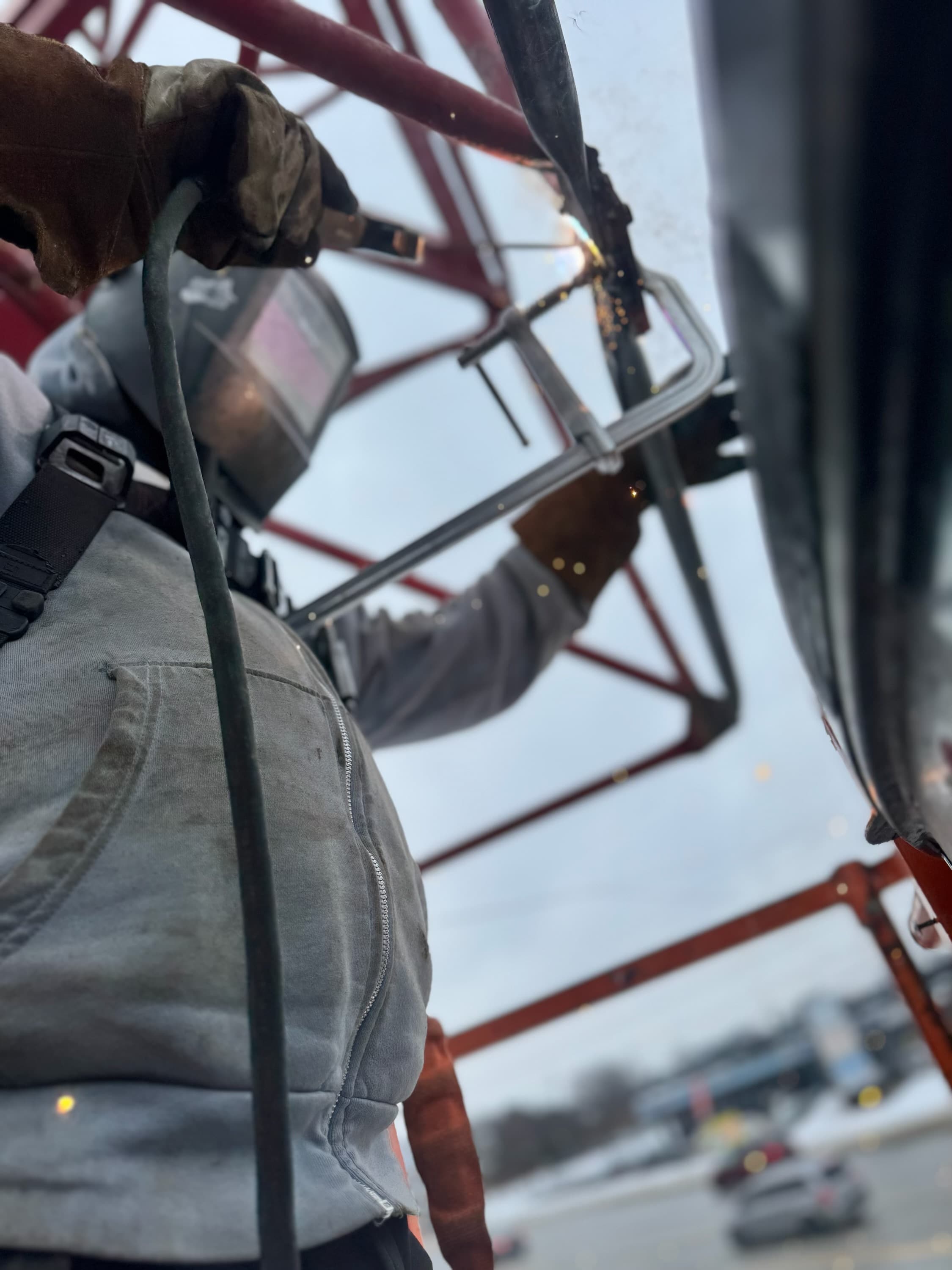 Welder in a mask and gloves works on a red metal structure with sparks flying.