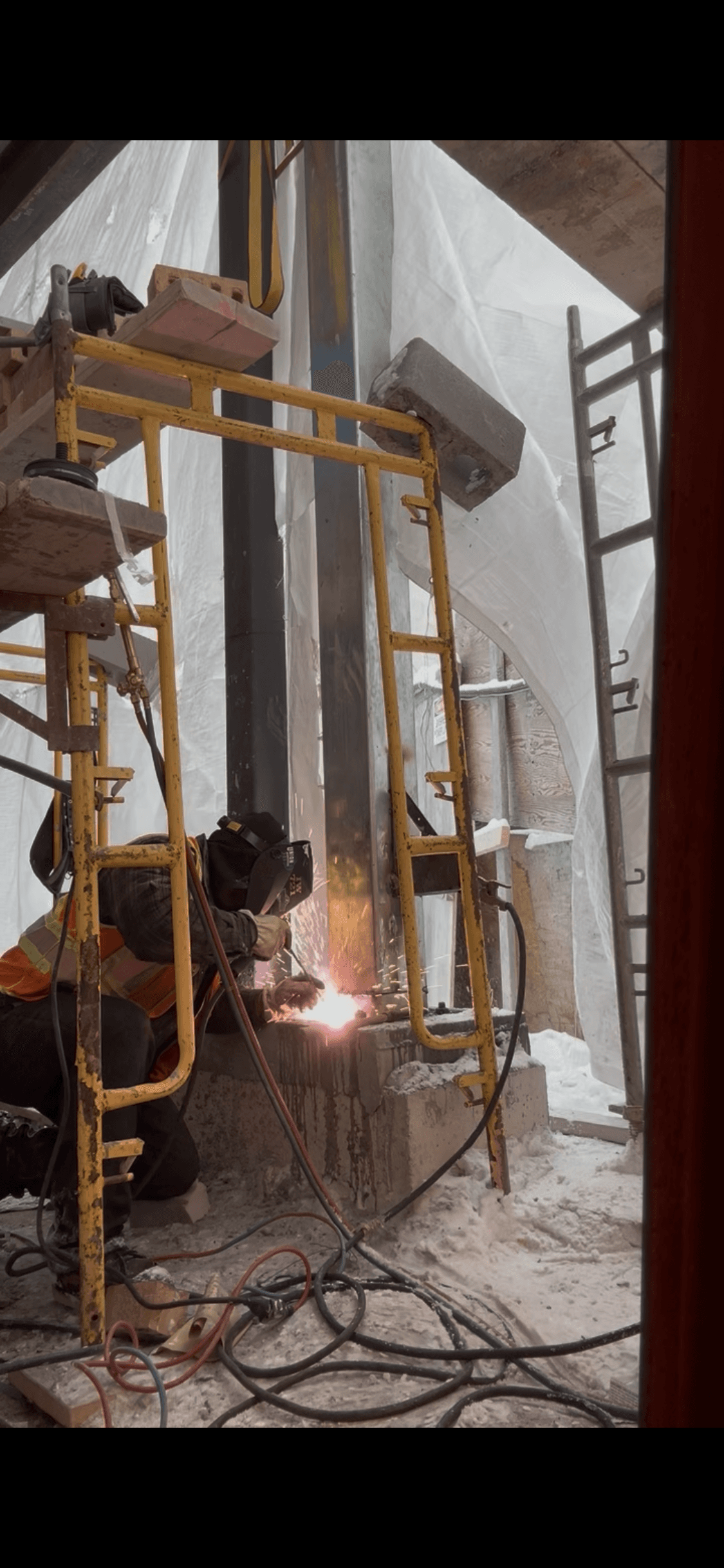 Construction worker in safety gear welds a steel beam on a snowy site with sparks.